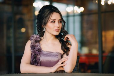 Restoran pencerelerinin önünde oturan ve kameraya poz veren hoş, genç bir kadının yakın çekimi.