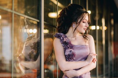 Çekici genç bir kadının portresi aşağı bakıyor, modern sürgülü restoran penceresine yaslanıyor. Pencereye yansıyan sevimli genç kadın.