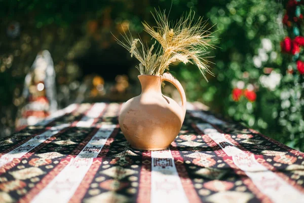 Closeup of bunch of dried wheat in clay vase on table in colorful garden in summer