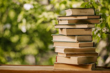 Ahşap tahtada, bulanık yeşil arka planı olan bir yığın eski kitap.