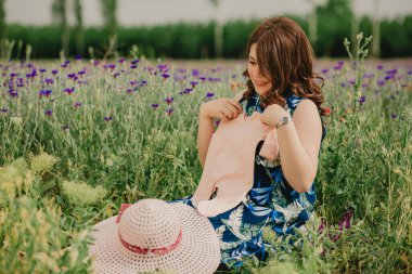 Genç annenin hamileliğin tadını çıkarırken ve bebek kıyafetlerini tutarken yakın plan.