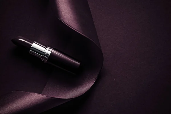 Lápiz labial de lujo y cinta de seda sobre fondo de vacaciones púrpura oscuro, maquillaje y cosméticos flatlay para el diseño de productos de la marca de belleza — Foto de Stock