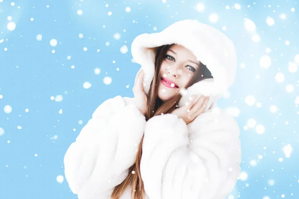 Natal e inverno férias retrato de jovem mulher de casaco de pele com capuz branco, neve no fundo azul, moda e estilo de vida — Fotografia de Stock