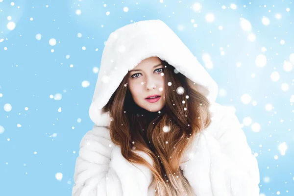 Natal e inverno férias retrato de jovem mulher de casaco de pele com capuz branco, neve no fundo azul, moda e estilo de vida — Fotografia de Stock