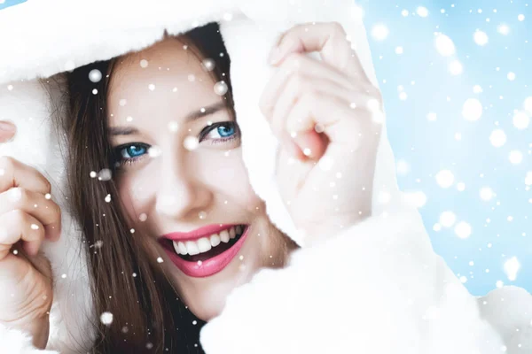 Natal e inverno férias retrato de jovem mulher de casaco de pele com capuz branco, neve no fundo azul, moda e estilo de vida — Fotografia de Stock