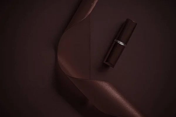 Lápiz labial de lujo y cinta de seda sobre fondo de vacaciones de chocolate, maquillaje y cosméticos flatlay para el diseño de productos de la marca de belleza — Foto de Stock