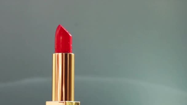 Розкішна червона помада в золотій трубці на кольоровому фоні і блискучі спалахи світла, розкішний макіяж і святкова косметика для бренду краси — стокове відео