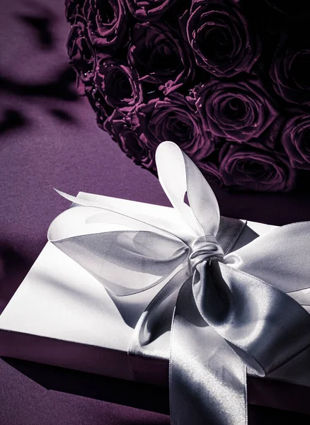 Caixa de presente de seda de férias de luxo e buquê de rosas em fundo roxo, surpresa romântica e flores como presente de aniversário ou dia dos namorados — Fotografia de Stock