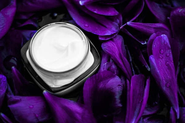 Розкішний крем-зволожувач для обличчя для шкіри обличчя на фіолетовому квітковому тлі, квіткова сутність, спа-косметика та косметична емульсія для продукту бренду skincare — стокове фото