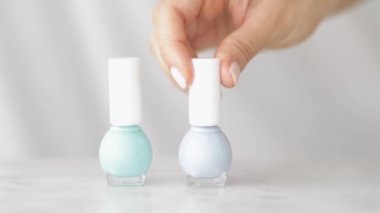 Doğal güzellik ürünü sahnesi, Fransız manikürü için kadın eli ve tırnak cilası şişeleri mermer masa üzerinde renkli pastel oje, makyaj ve kozmetik marka.