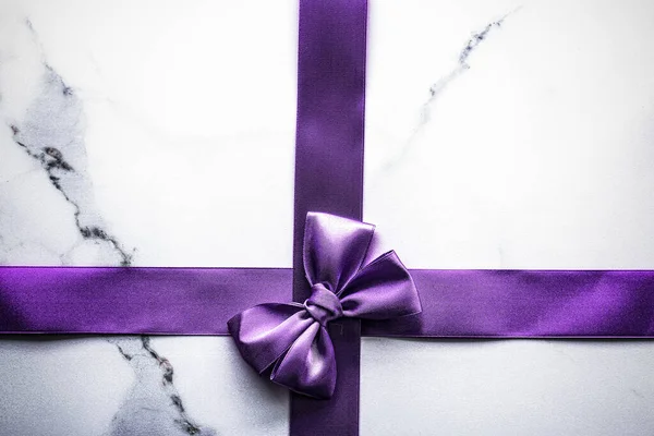 Purple silk ribbon and bow on luxury marble background, holiday flatlay backdrop