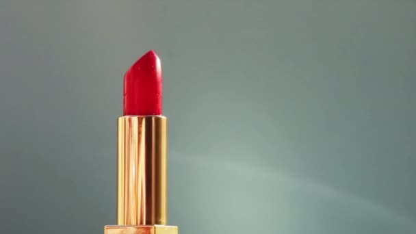 Luxuriöser roter Lippenstift in goldener Röhre auf farbigem Hintergrund und leuchtenden Lichterketten, Luxus-Make-up-Produkt und Urlaubskosmetik für Beauty-Marken — Stockvideo