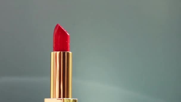 Розкішна червона помада в золотій трубці на кольоровому фоні і блискучі спалахи світла, розкішний макіяж і святкова косметика для бренду краси — стокове відео