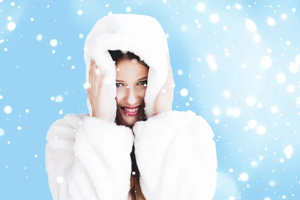 Natal e inverno férias retrato de jovem mulher de casaco de pele com capuz branco, neve no fundo azul, moda e estilo de vida — Fotografia de Stock