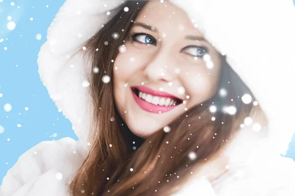 Christmas and winter holiday portrait of young woman in white hooded fur coat, snow on blue background, fashion and lifestyle — Stock Photo, Image