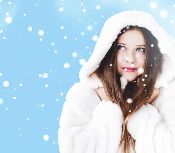 Natal e inverno férias retrato de jovem mulher de casaco de pele com capuz branco, neve no fundo azul, moda e estilo de vida — Fotografia de Stock