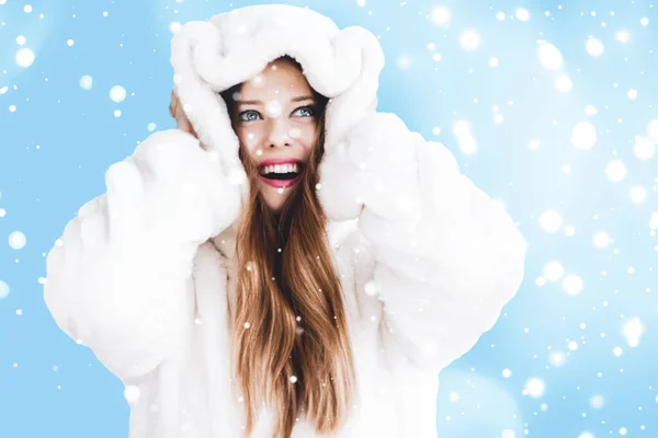 Natal e inverno férias retrato de jovem mulher de casaco de pele com capuz branco, neve no fundo azul, moda e estilo de vida — Fotografia de Stock