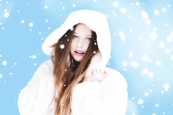 Natal e inverno férias retrato de jovem mulher de casaco de pele com capuz branco, neve no fundo azul, moda e estilo de vida — Fotografia de Stock