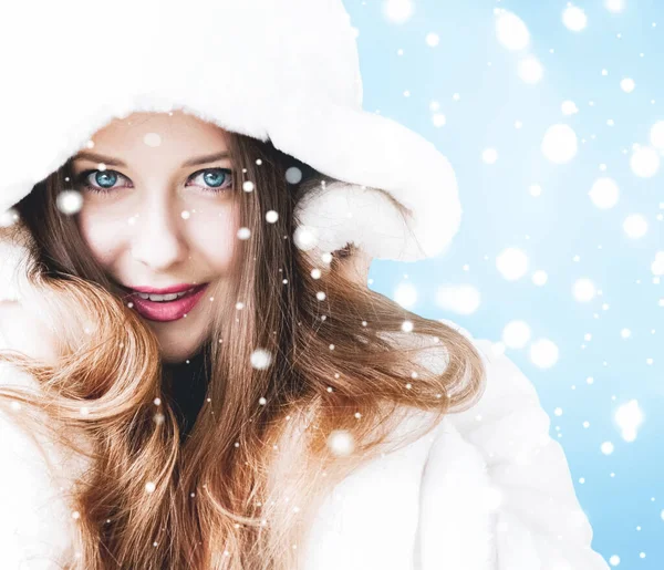 Natal e inverno férias retrato de jovem mulher de casaco de pele com capuz branco, neve no fundo azul, moda e estilo de vida — Fotografia de Stock