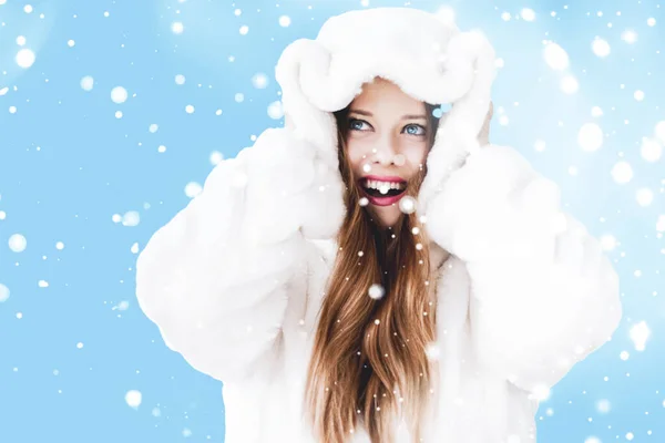 Christmas and winter holiday portrait of young woman in white hooded fur coat, snow on blue background, fashion and lifestyle — Stock Photo, Image