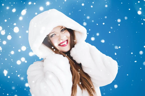 Feliz Navidad y vacaciones de invierno retrato de mujer joven con capucha blanca abrigo de piel, nieve sobre fondo azul, moda y estilo de vida — Foto de Stock