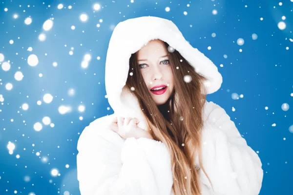 Feliz Natal e férias de inverno retrato de jovem mulher de casaco de pele com capuz branco, neve no fundo azul, moda e estilo de vida — Fotografia de Stock