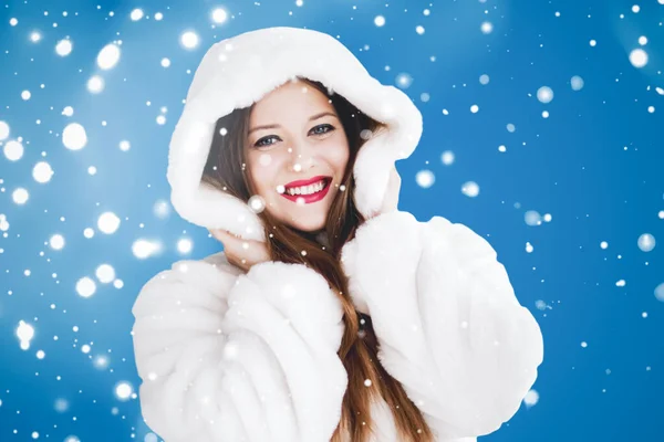 Feliz Natal e férias de inverno retrato de jovem mulher de casaco de pele com capuz branco, neve no fundo azul, moda e estilo de vida — Fotografia de Stock