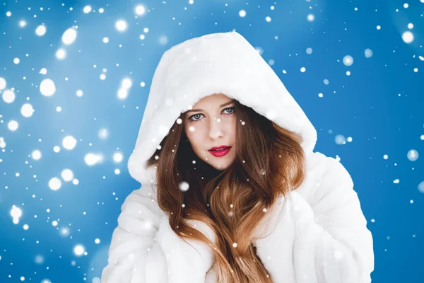 Happy Christmas and winter holiday portrait of young woman in white hooded fur coat, snow on blue background, fashion and style — Stok Foto