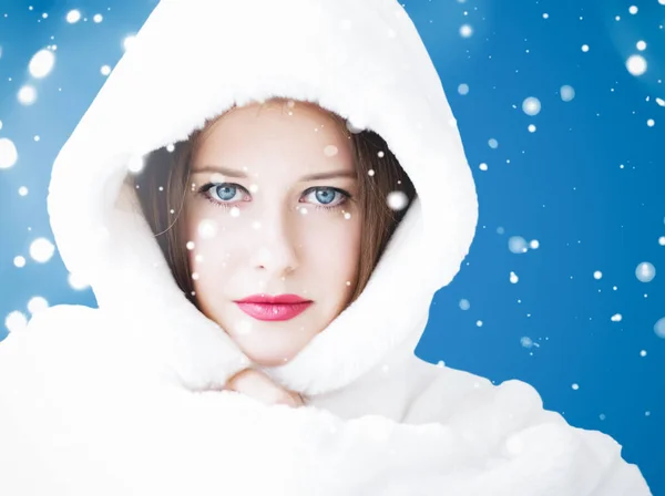 Feliz Natal e férias de inverno retrato de jovem mulher de casaco de pele com capuz branco, neve no fundo azul, moda e estilo de vida — Fotografia de Stock