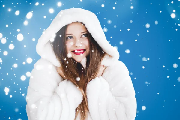 Feliz Natal e férias de inverno retrato de jovem mulher de casaco de pele com capuz branco, neve no fundo azul, moda e estilo de vida — Fotografia de Stock
