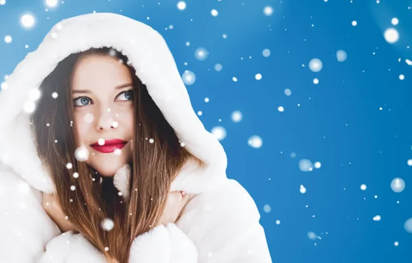 Feliz Navidad y vacaciones de invierno retrato de mujer joven con capucha blanca abrigo de piel, nieve sobre fondo azul, moda y estilo de vida — Foto de Stock