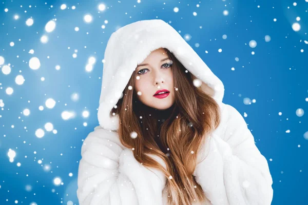 Feliz Natal e férias de inverno retrato de jovem mulher de casaco de pele com capuz branco, neve no fundo azul, moda e estilo de vida — Fotografia de Stock