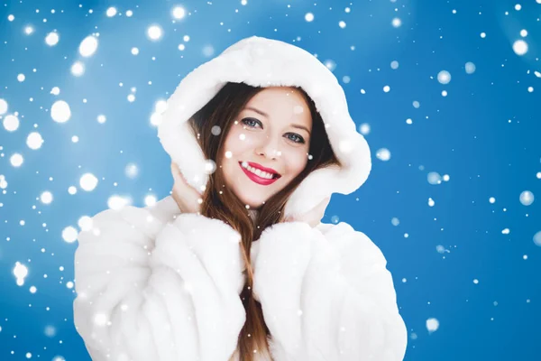 Feliz Navidad y vacaciones de invierno retrato de mujer joven con capucha blanca abrigo de piel, nieve sobre fondo azul, moda y estilo de vida — Foto de Stock