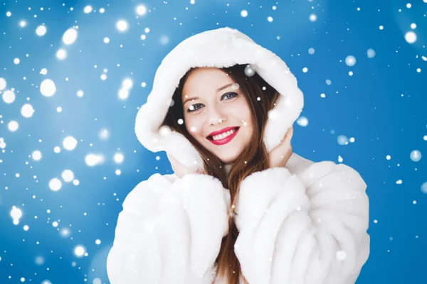 Feliz Natal e férias de inverno retrato de jovem mulher de casaco de pele com capuz branco, neve no fundo azul, moda e estilo de vida — Fotografia de Stock