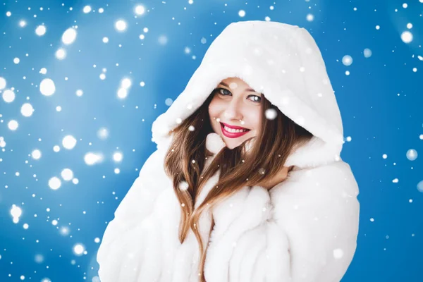 Feliz Navidad y vacaciones de invierno retrato de mujer joven con capucha blanca abrigo de piel, nieve sobre fondo azul, moda y estilo de vida — Foto de Stock