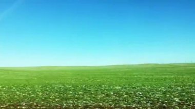 Yeşil arazi ve mavi gökyüzü, güneşli bir günde bir doğa manzarasının yanından geçiyor.