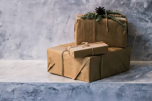 Holiday delivery boxes, parcels wrapped in brown paper, decorated and tied with rough twine, stone background with copyspace