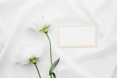 Düğün davetiyesi ya da hediye kartı ve beyaz gül çiçekleri düğün arkaplanı olarak düz kumaş üzerinde, boş kağıt ve tatil damgası, düz dizayn