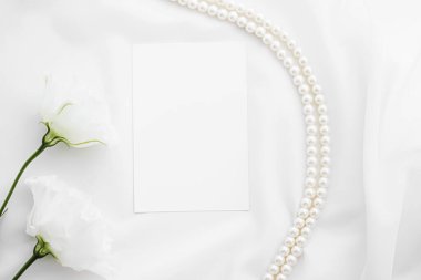 Düğün davetiyesi, beyaz gül çiçekleri ve inciler düğün arkaplanı olarak ipek kumaş üzerinde, boş kağıt tebrik kartı ve tatil markası, düz dizayn