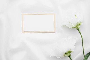 Düğün davetiyesi ya da hediye kartı ve beyaz gül çiçekleri düğün arkaplanı olarak düz kumaş üzerinde, boş kağıt ve tatil damgası, düz dizayn