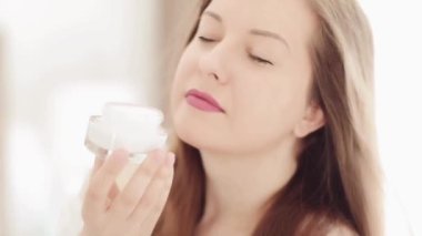 Doğal cilt bakımı rutini, güzel bir kadın gülümseyen ve elinde yüz nemlendirici kremi kavanozu olan sağlıklı cilt bakımı, lüks kozmetik ürünleri, sağlıklı insanlar ve güzellik tedavisi.