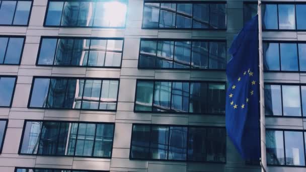 Bandiera dell'Unione europea sventola davanti al moderno edificio degli uffici aziendali, simbolo del Parlamento europeo, della Commissione e del Consiglio — Video Stock