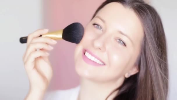 Γυναίκα με πινέλο μακιγιάζ και compact καθρέφτη που εφαρμόζει καλλυντική πούδρα και χαμογελά, προσωπογραφία του όμορφου μοντέλου σε ροζ φόντο, φυσική ιδέα make-up, καλλυντικά και προϊόντα περιποίησης δέρματος εμπορική — Αρχείο Βίντεο