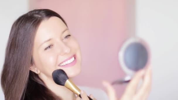 Vrouw met make-up borstel en compacte spiegel aanbrengen cosmetische poeder en glimlachen, gezicht portret van mooi model op roze achtergrond, natuurlijke make-up idee, cosmetica en huidverzorgingsproduct commerciële — Stockvideo