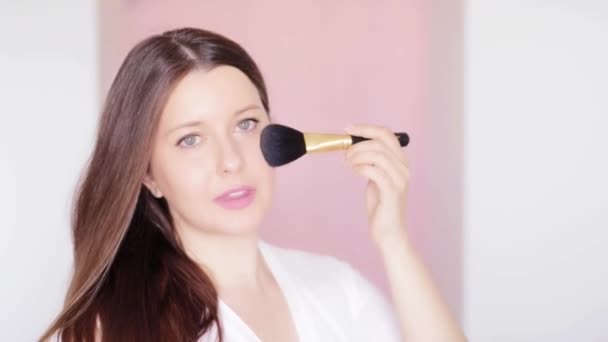 Mujer con cepillo cosmético aplicando maquillaje y sonrisa, retrato facial de belleza de modelo femenino caucásico sobre fondo rosa, idea de maquillaje natural, cosméticos y productos para el cuidado de la piel comercial — Vídeo de stock