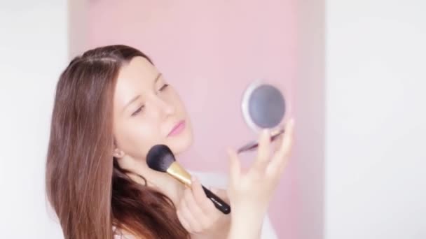Vrouw met make-up borstel en compacte spiegel aanbrengen cosmetische poeder en glimlachen, gezicht portret van mooi model op roze achtergrond, natuurlijke make-up idee, cosmetica en huidverzorgingsproduct commerciële — Stockvideo