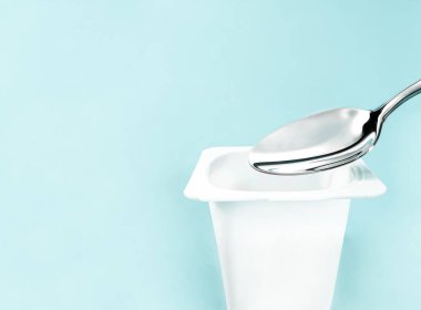 Yoğurt kabı ve nane arkaplanda gümüş kaşık yoğurt kremalı beyaz plastik kap sağlıklı beslenme ve beslenme dengesi için taze süt ürünü.