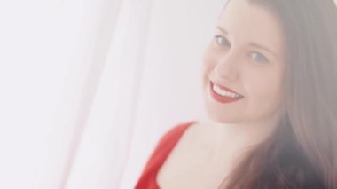 Güzel esmer kadın gülümsüyor, poz veriyor ve dans ediyor, pencereden veya kapıdan parlak bir ışık ve arka planda beyaz perdeler, kadınsı yaşam tarzı ve doğal güzellik.