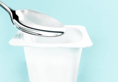 Yoğurt kabı ve nane arkaplanda gümüş kaşık yoğurt kremalı beyaz plastik kap sağlıklı beslenme ve beslenme dengesi için taze süt ürünü.