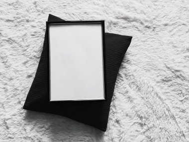 Poster fotokopisi olarak boş telif alanı olan ince ahşap çerçeve, siyah yastık ve yumuşak beyaz battaniye, düz arkaplan ve sanat ürünü